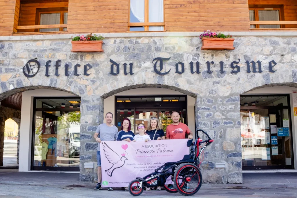 Paloma et sa famille posent devant l’Office de Tourisme avec la banderole de l’association et le fauteuil tout-terrain Hippocampe.