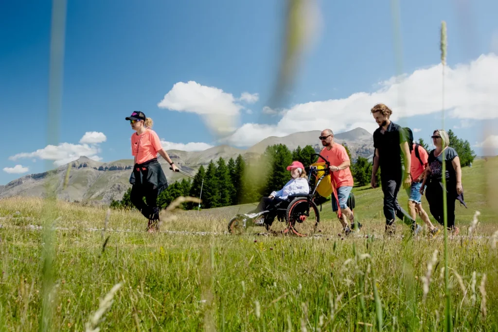 Plusieurs personnes en randonnée à Valberg en été, accompagnant un fauteuil tout-terrain Hippocampe.